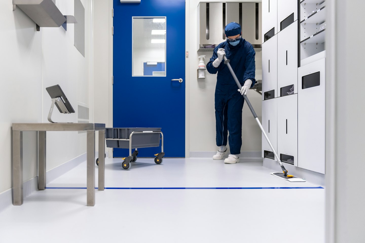 Mitarbeiter in blauer Reinraumkleidung wischt einen sterilen Laborboden.